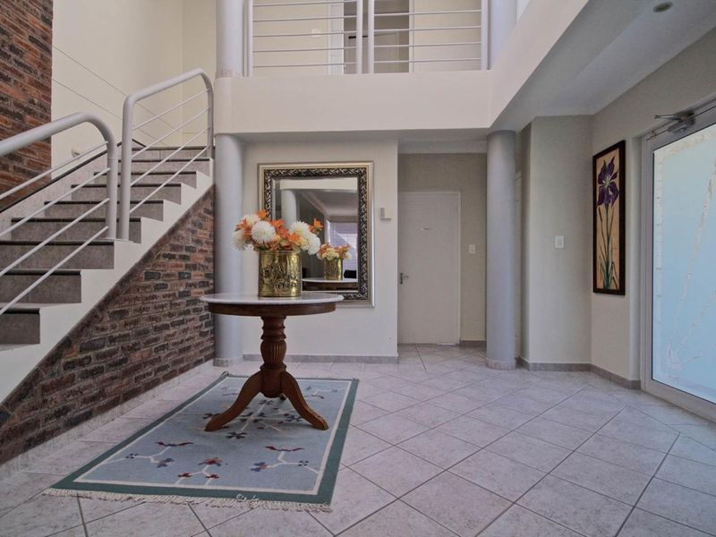 Spacious double-volume entrance hall featuring a striking exposed brick staircase, tiled flooring, and modern architectural columns.