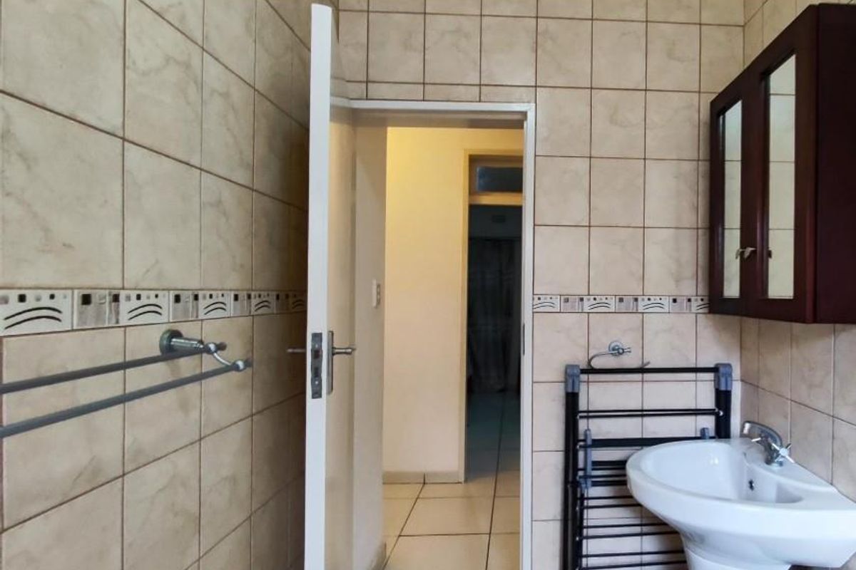 A functional bathroom featuring wall-mounted basin, vanity cabinet, and tiled walls, providing a practical space with potential for modern updates.