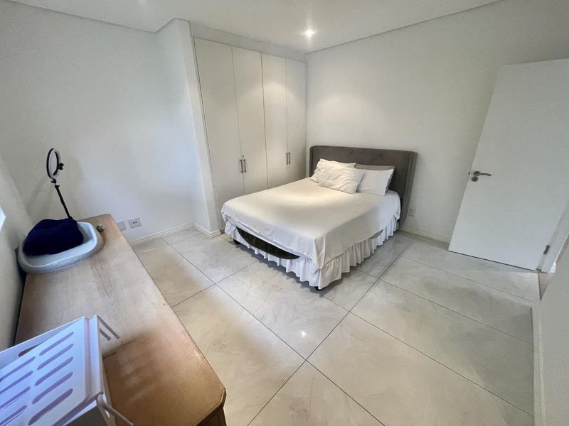 A bright, modern bedroom featuring large format floor tiles, built-in cupboards, and recessed ceiling lighting.