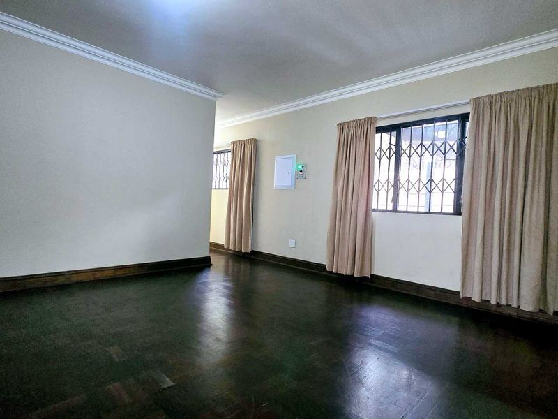 Spacious living area featuring dark parquet flooring, neutral walls, and security gates on the windows.