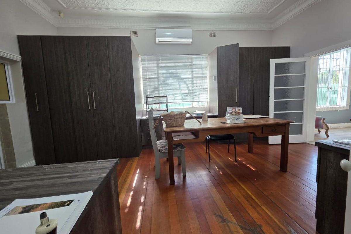 Spacious office or bedroom featuring polished timber flooring, built-in dark wood cabinetry, decorative ceiling cornices, and a wall-mounted air conditioning unit.