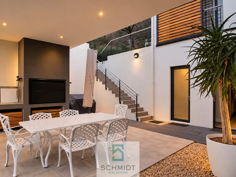 A modern covered patio featuring a built-in braai, outdoor sink, and direct access to an external staircase, perfect for outdoor entertaining.