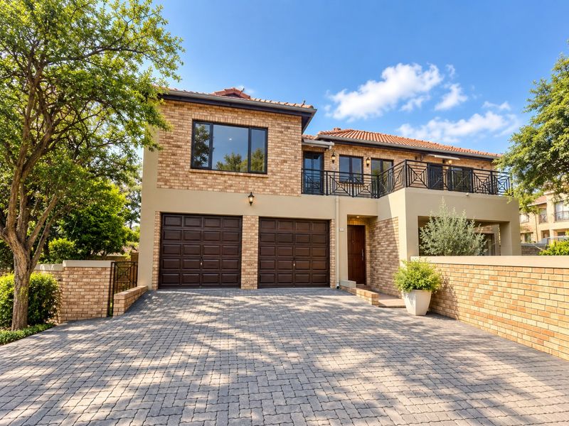 A well-maintained double-story townhouse featuring a paved driveway, double garage, and an upper-level balcony with brick and plaster finishes.