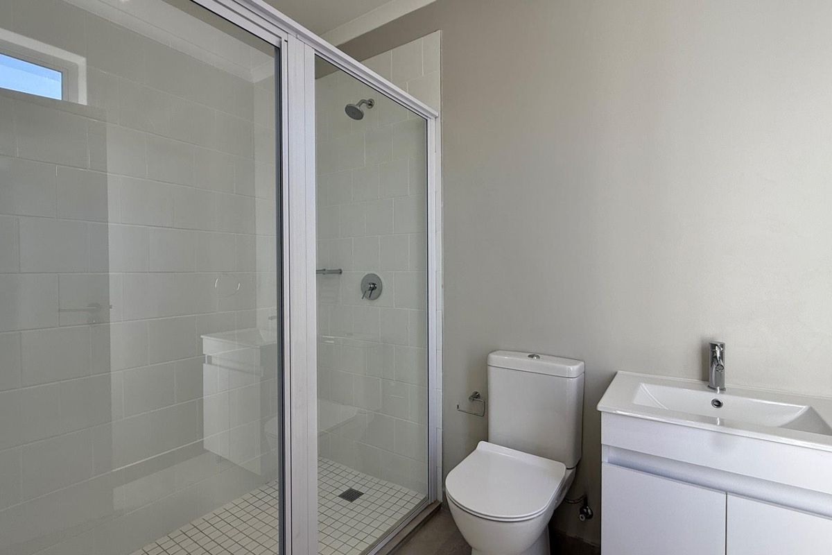 A clean, modern bathroom featuring a glass-enclosed shower, a white vanity with basin, and a standard toilet with neutral wall finishes.