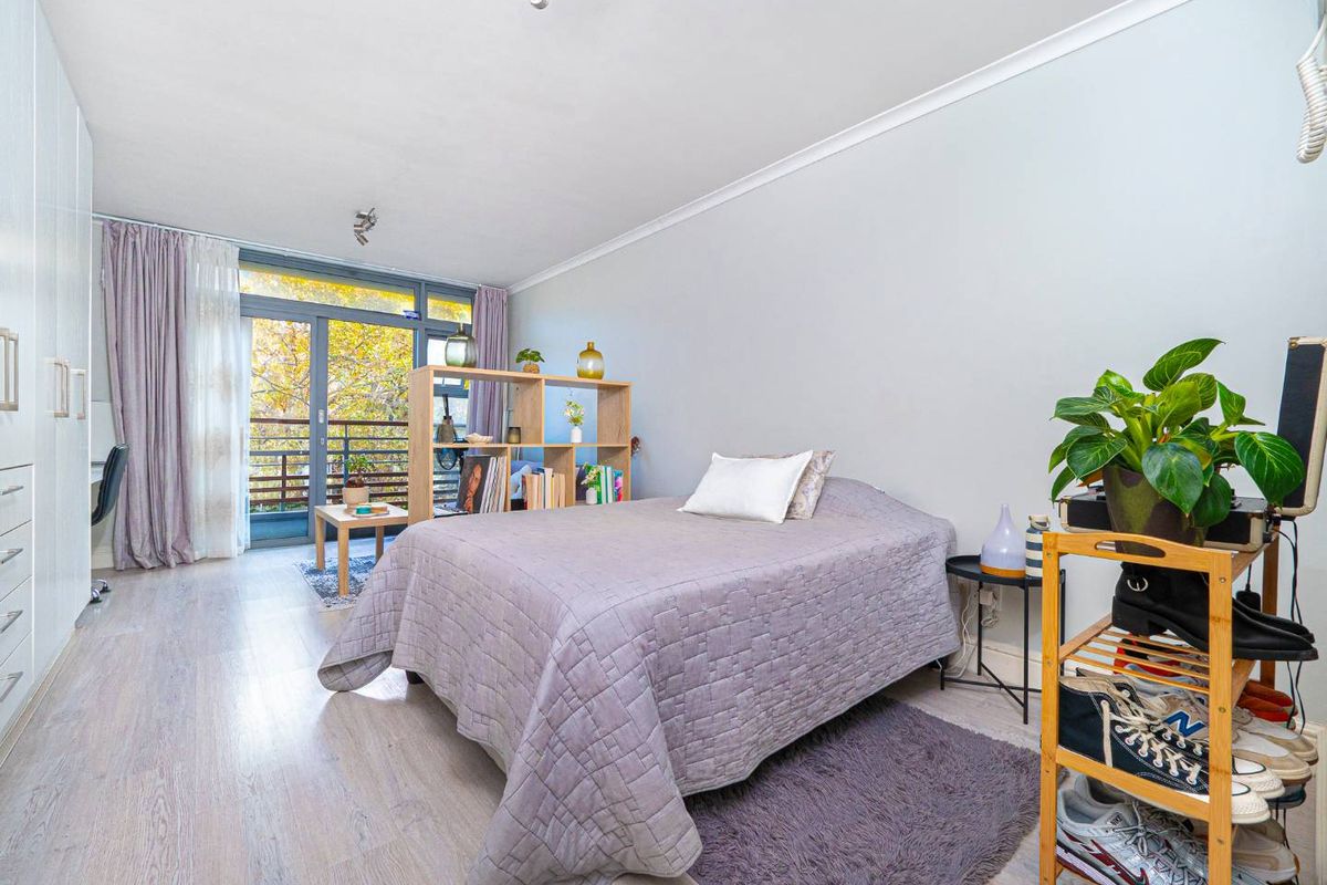 A bright bedroom featuring light wood-look flooring, built-in wardrobes, and large glass sliding doors leading to a private balcony.