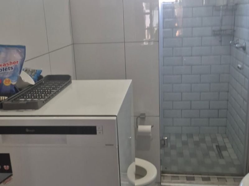 A functional bathroom featuring a glass-enclosed shower with subway tile finishes and modern laminate flooring.