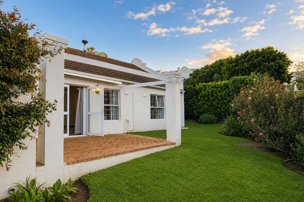 A well-maintained rear exterior view of the townhouse featuring a brick-paved patio, pergola structure, and a lush, landscaped garden.