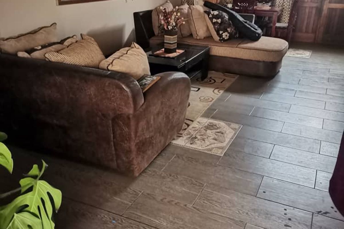 A living room featuring dark wood-look tiled flooring with decorative inset tiles, a large wall mirror, and access to an adjacent room.