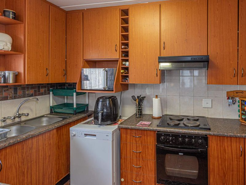 A functional kitchen featuring wood-look laminate cabinetry, tiled backsplash, built-in oven, electric hob, and a double bowl stainless steel sink.