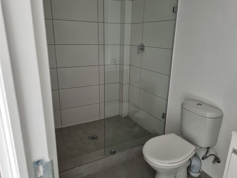 A clean, modern bathroom featuring a glass-enclosed shower with tiled walls and a standard toilet.