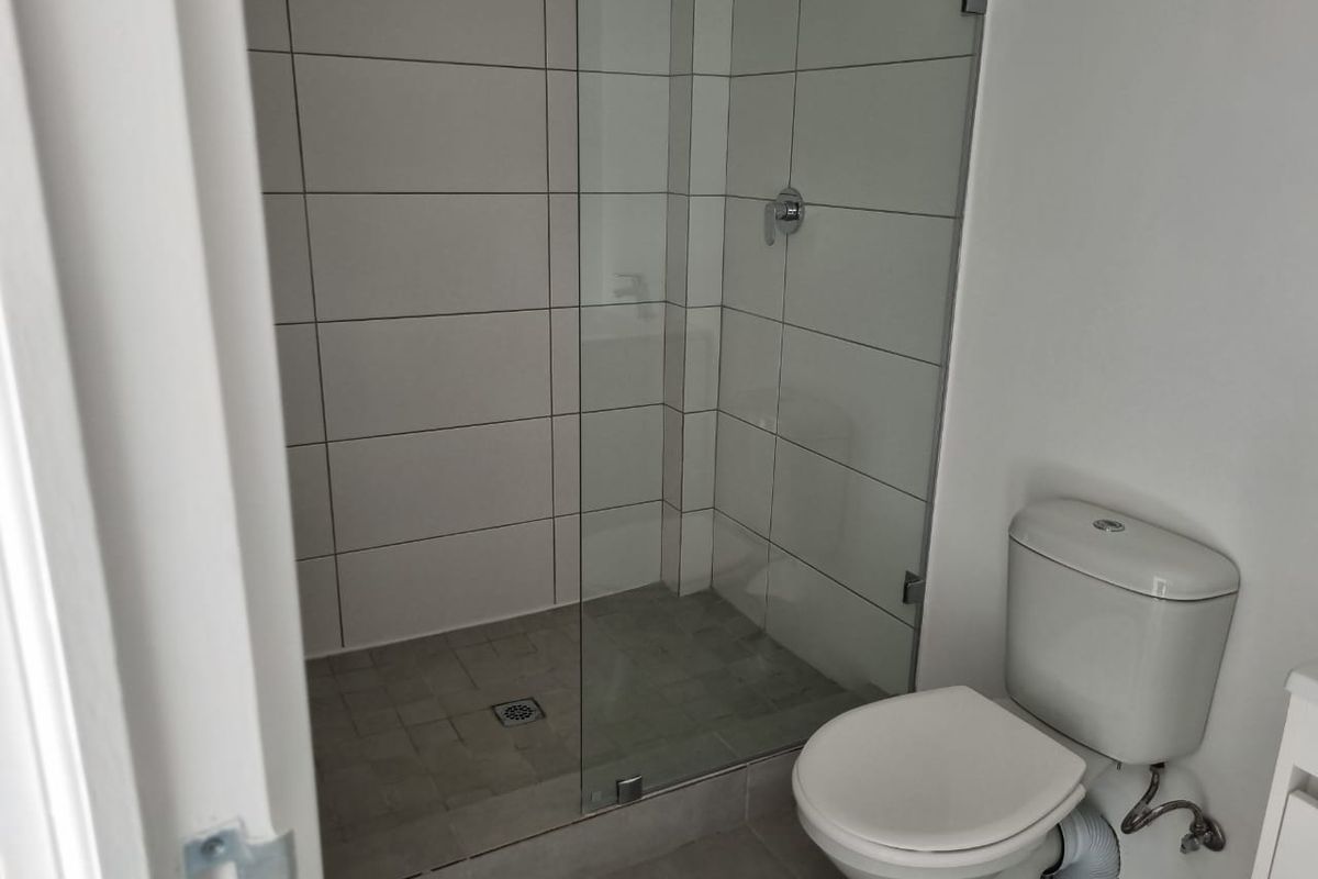 A clean, modern bathroom featuring a glass-enclosed shower with tiled walls and a standard toilet.
