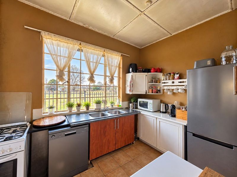 A functional kitchen featuring a double basin sink, tiled flooring, and ample cabinetry, with a large window providing natural light and garden views.