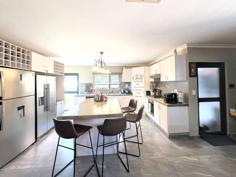 Spacious modern kitchen featuring a large central island, ample built-in cabinetry, integrated appliances, and sleek tiled flooring throughout.