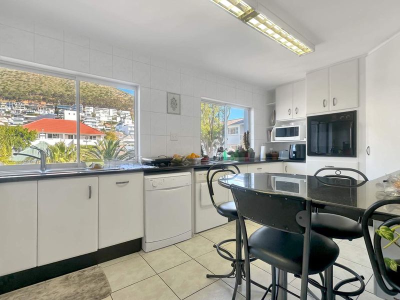A functional kitchen featuring white cabinetry, granite countertops, built-in oven, and large windows providing natural light and scenic views.