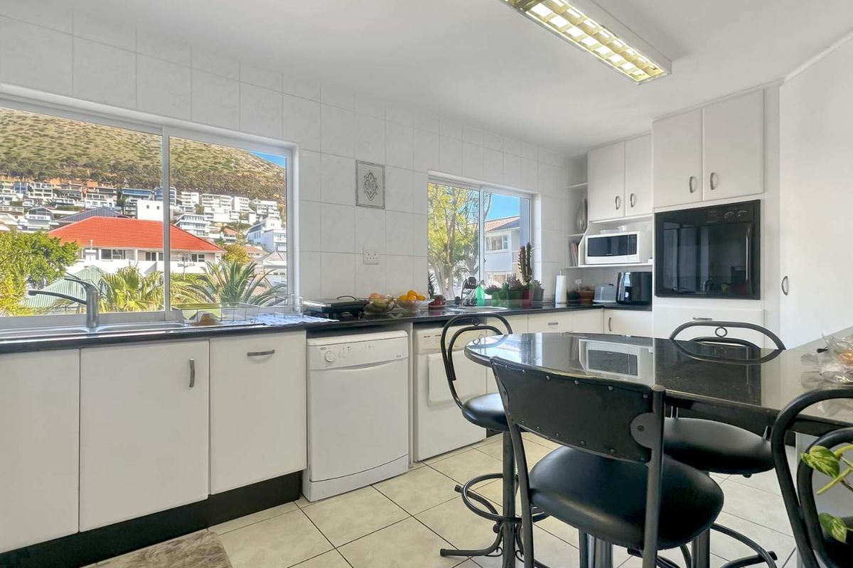 A functional kitchen featuring white cabinetry, granite countertops, built-in oven, and large windows providing natural light and scenic views.