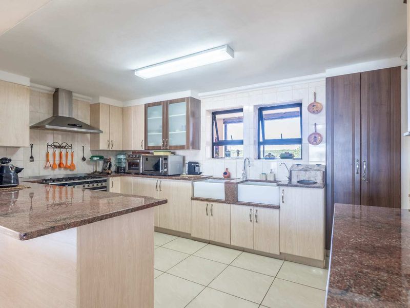 Spacious kitchen featuring granite countertops, double farmhouse sink, stainless steel extractor fan, and ample built-in cabinetry with tiled flooring.