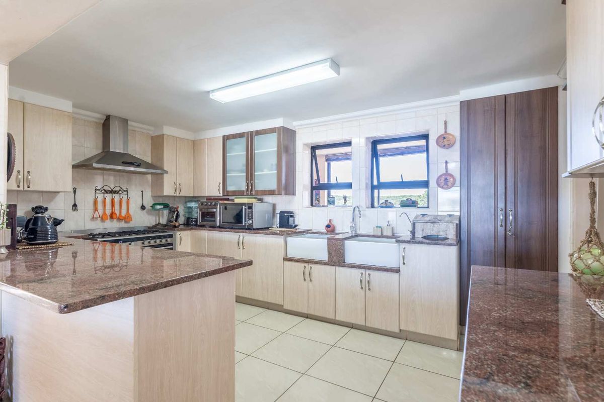 Spacious kitchen featuring granite countertops, double farmhouse sink, stainless steel extractor fan, and ample built-in cabinetry with tiled flooring.