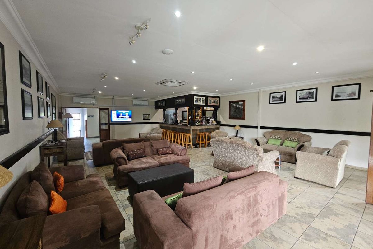 Spacious hotel lounge area featuring a built-in bar counter, recessed ceiling lighting, and tiled flooring, providing a comfortable communal space for guests.