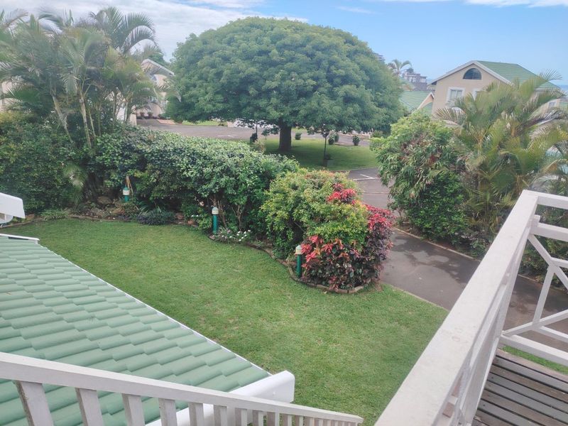 Elevated view overlooking a well-maintained garden, green tiled roof, and surrounding residential estate grounds.