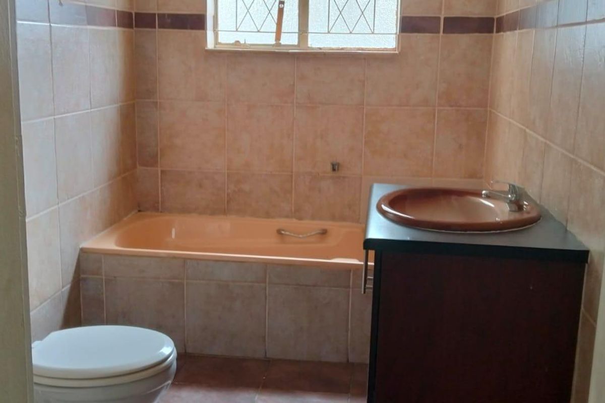 A dated bathroom featuring a built-in bathtub, a vanity with a basin, and tiled walls. The space requires modernization to improve its aesthetic appeal.