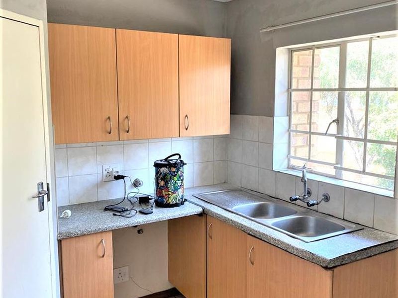 A functional kitchen featuring laminate cabinetry, a double bowl stainless steel sink, tiled splashback, and ceramic floor tiles with security bars on the window.