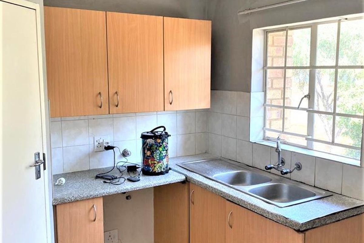 A functional kitchen featuring laminate cabinetry, a double bowl stainless steel sink, tiled splashback, and ceramic floor tiles with security bars on the window.