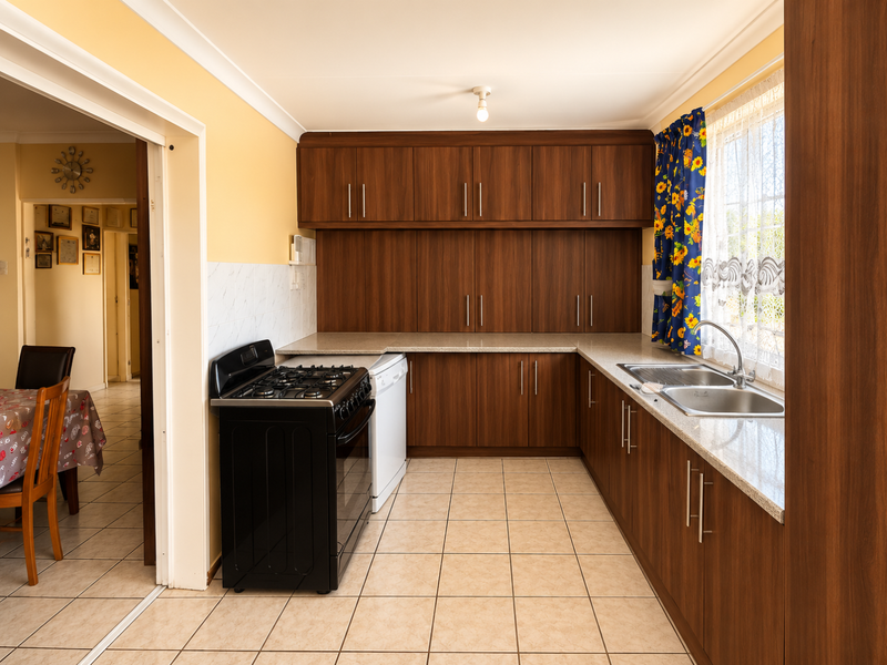 Functional kitchen featuring wood-finish cabinetry, laminate countertops, a stainless steel double sink, and tiled flooring, with an adjacent dining area visible.