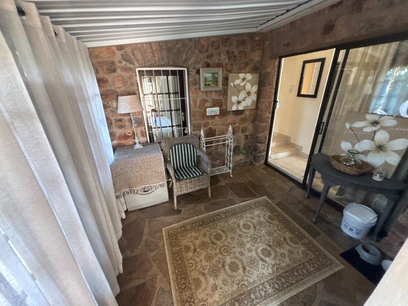 A covered patio area featuring rustic stone wall cladding, flagstone flooring, and a sliding glass door providing access to the interior.