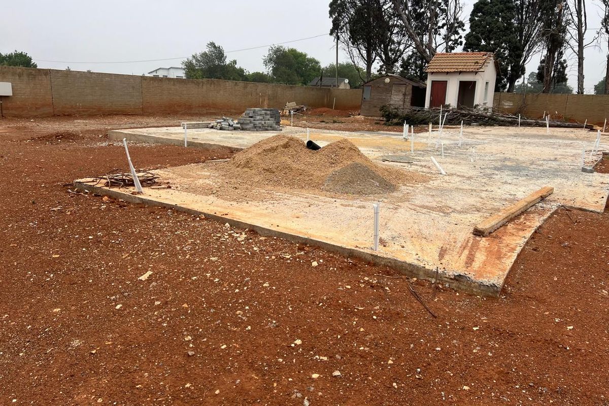 Vacant residential land featuring a concrete slab foundation, perimeter boundary wall, and existing plumbing rough-ins, ready for further development.