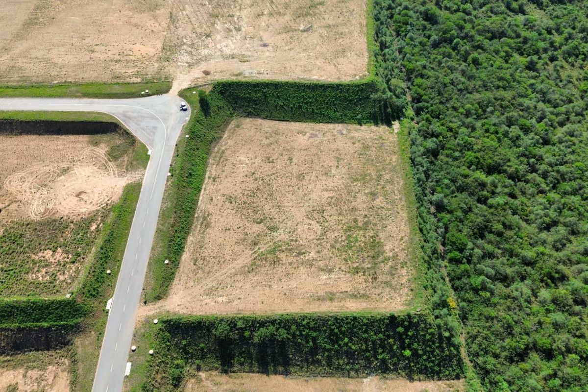 Aerial view of a cleared industrial land parcel featuring paved road access and established perimeter embankments adjacent to a wooded area.