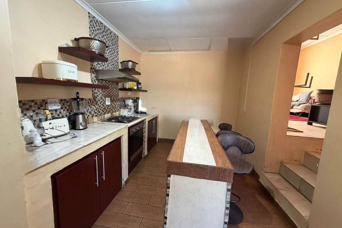 A functional kitchen featuring built-in cabinetry, a tiled breakfast bar, integrated oven and hob, and mosaic tile backsplash with tiled flooring.