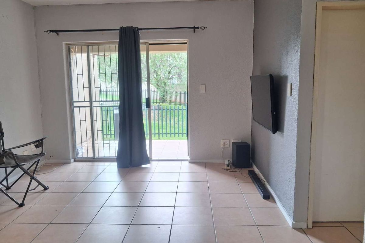 A living room featuring tiled flooring and a sliding glass door with a security gate, providing direct access to the outdoor area.