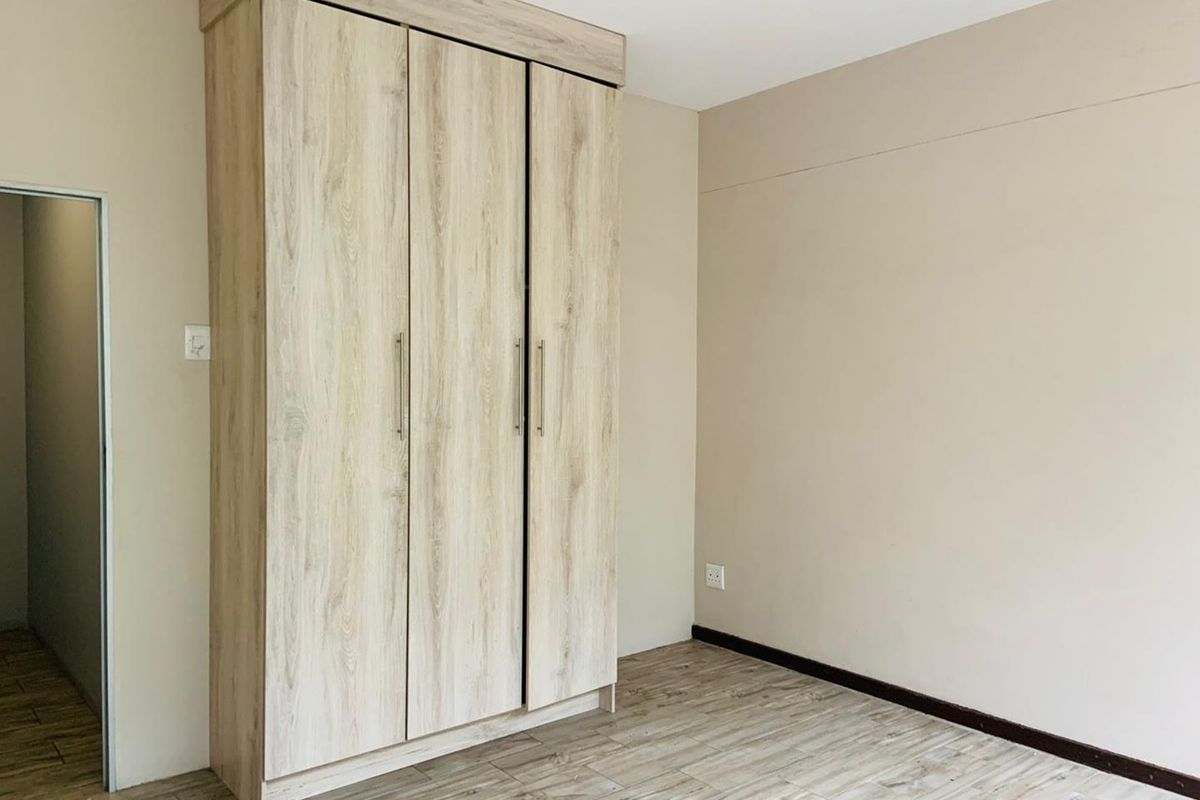 A bright bedroom featuring light wood-look flooring and a modern, built-in triple wardrobe with a matching wood-grain finish.