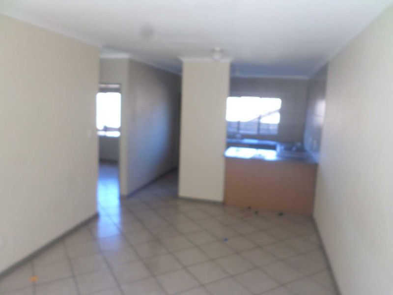 An open-plan living and kitchen area featuring tiled flooring and built-in kitchen cabinetry in a vacant apartment setting.