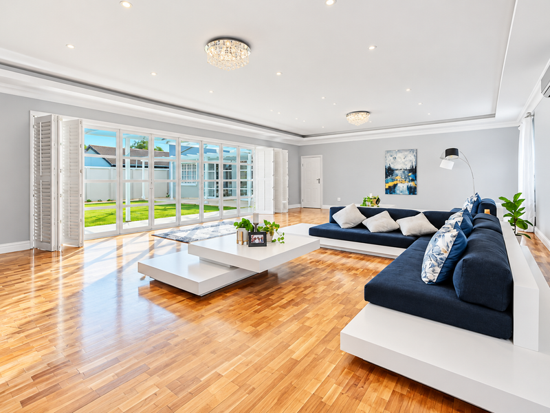 Spacious living room featuring polished hardwood floors, recessed lighting, and expansive bi-fold glass doors that open to a manicured garden.