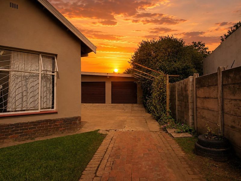 Rear exterior view of the property featuring a double garage, brick paved driveway, and precast concrete boundary wall at sunset.