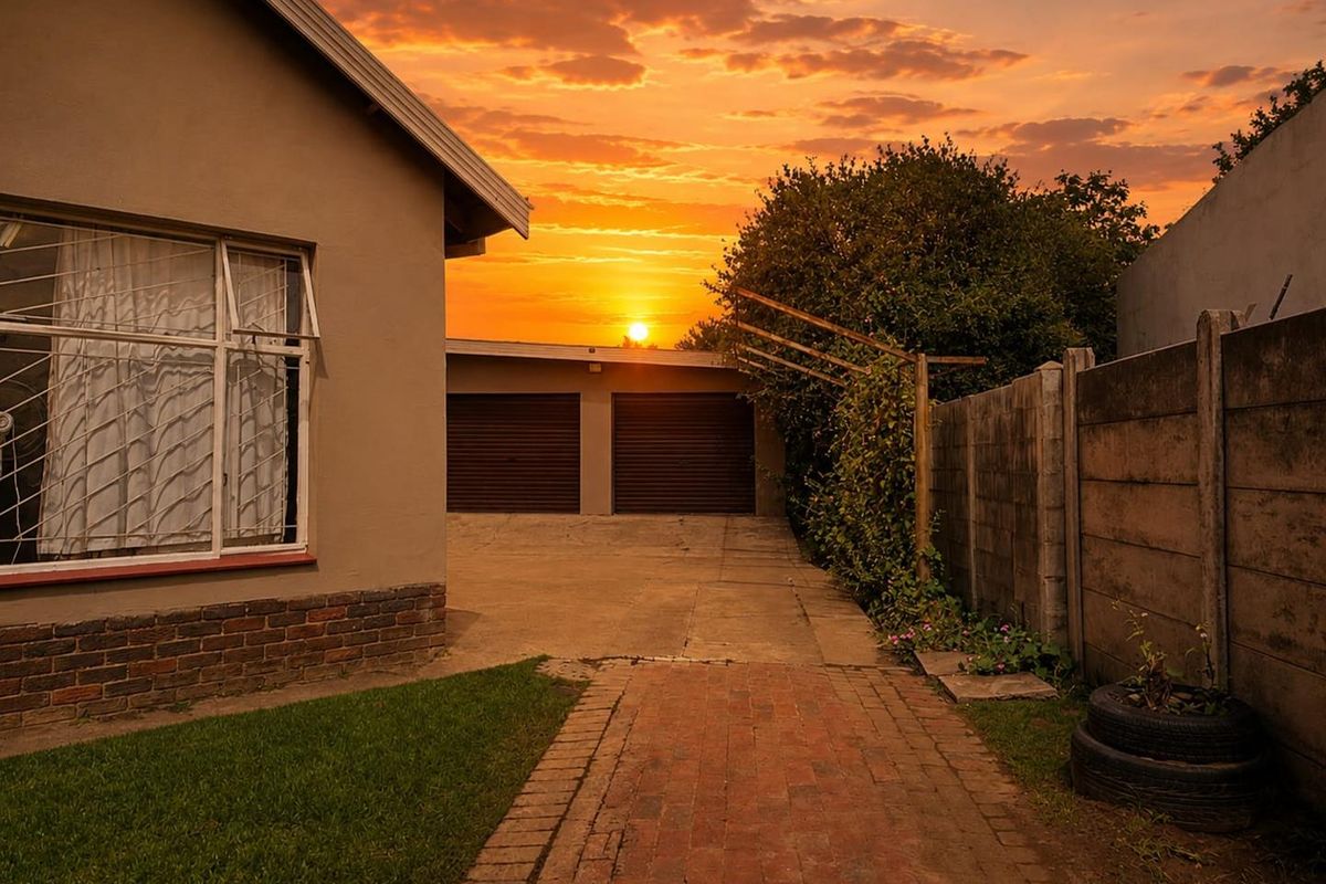 Rear exterior view of the property featuring a double garage, brick paved driveway, and precast concrete boundary wall at sunset.