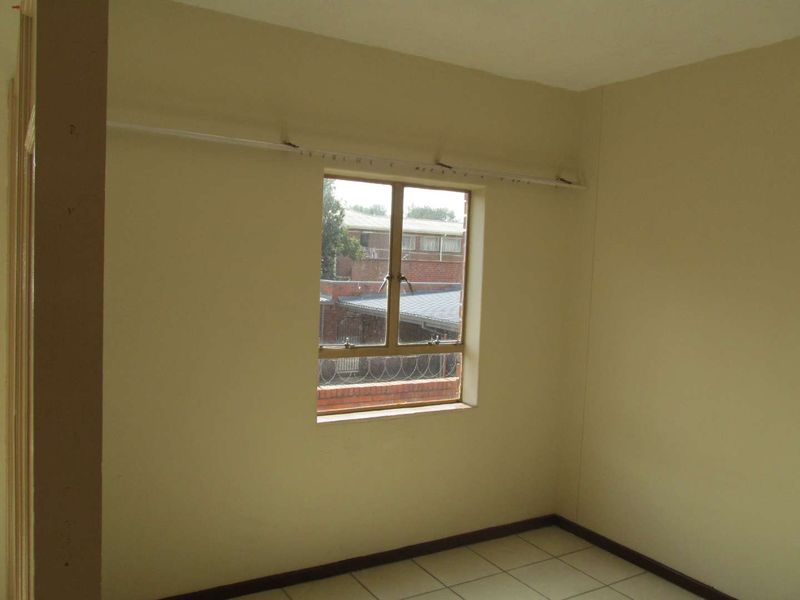 An empty bedroom featuring tiled flooring and a single casement window, presenting a blank canvas for potential renovation or interior design updates.