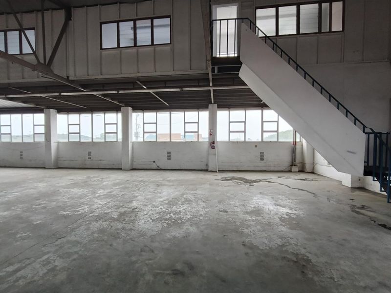 Spacious industrial utility area featuring concrete flooring, a mezzanine level with a steel staircase, and large windows providing ample natural light.