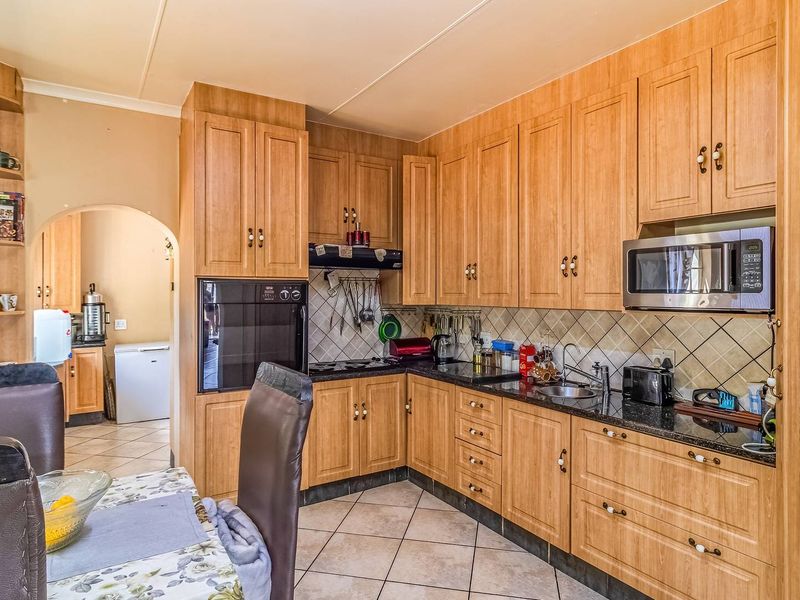 A functional kitchen featuring wood-finish cabinetry, granite countertops, built-in oven and microwave, and tiled flooring, with an adjacent scullery area visible through the archway.