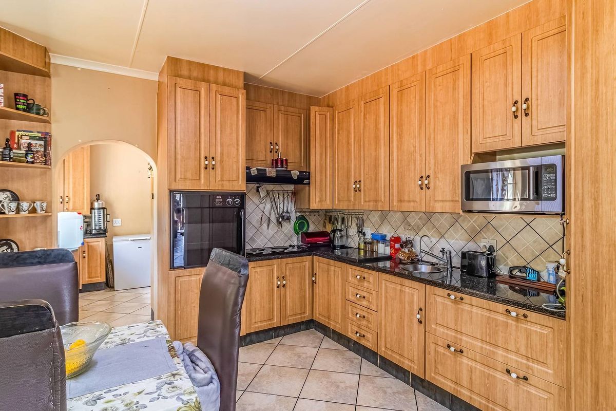 A functional kitchen featuring wood-finish cabinetry, granite countertops, built-in oven and microwave, and tiled flooring, with an adjacent scullery area visible through the archway.