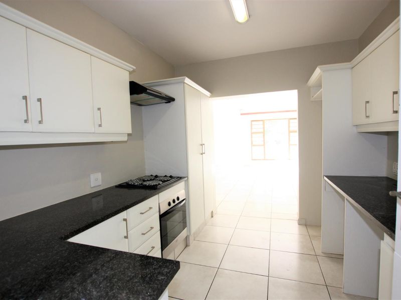 A clean, functional kitchen featuring white cabinetry, dark granite countertops, a built-in oven, gas hob, and tiled flooring.