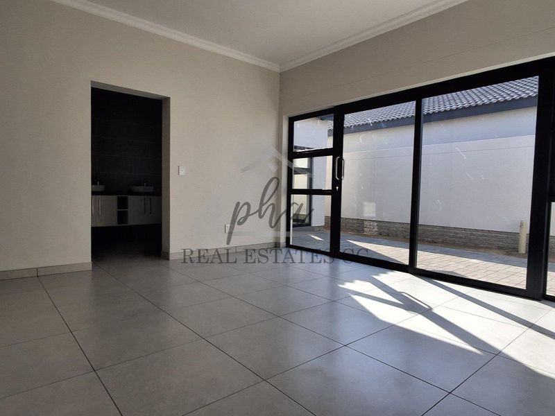 A bright, empty living area featuring large format floor tiles, coved ceilings, and expansive sliding glass doors leading to an outdoor paved area.