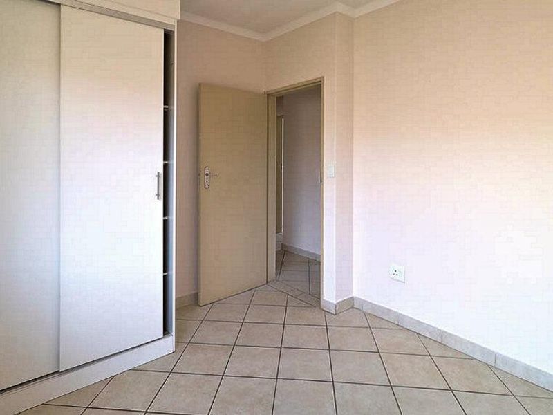 An empty bedroom featuring neutral walls, tiled flooring, and a built-in sliding door wardrobe.