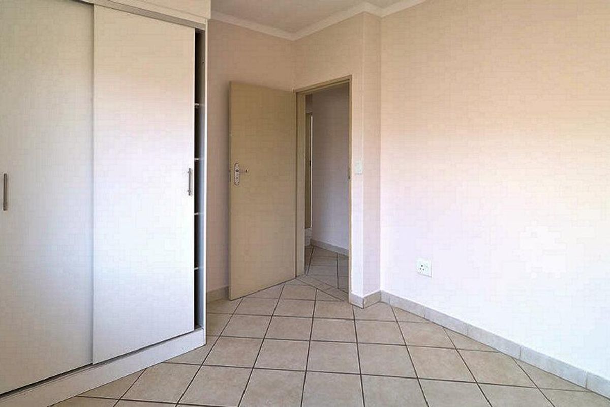 An empty bedroom featuring neutral walls, tiled flooring, and a built-in sliding door wardrobe.