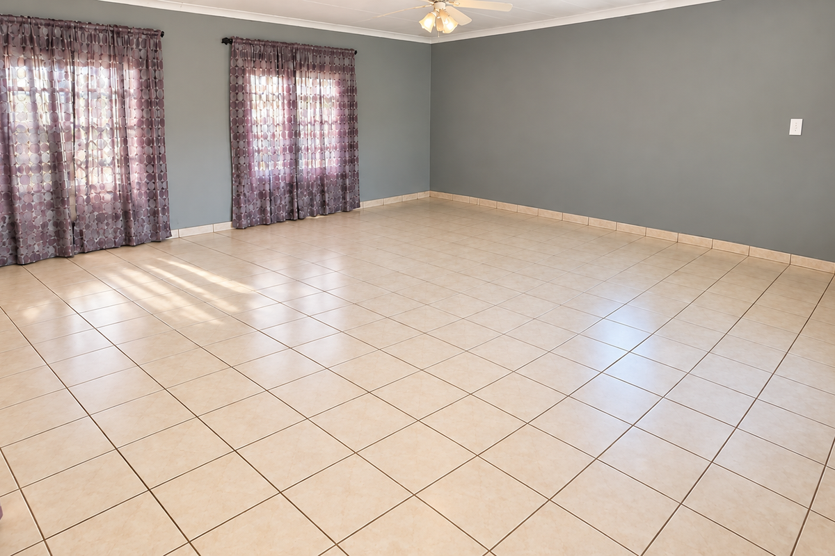 A spacious, empty living room featuring neutral ceramic tile flooring, grey walls, and a ceiling fan, offering a clean canvas for interior design.
