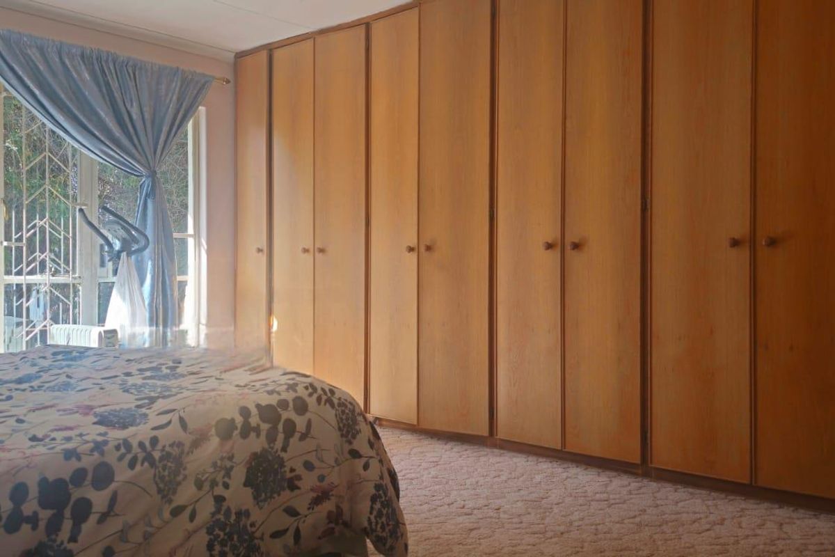 A bedroom featuring extensive floor-to-ceiling built-in wooden wardrobes and large windows with security bars, offering natural light and ample storage space.