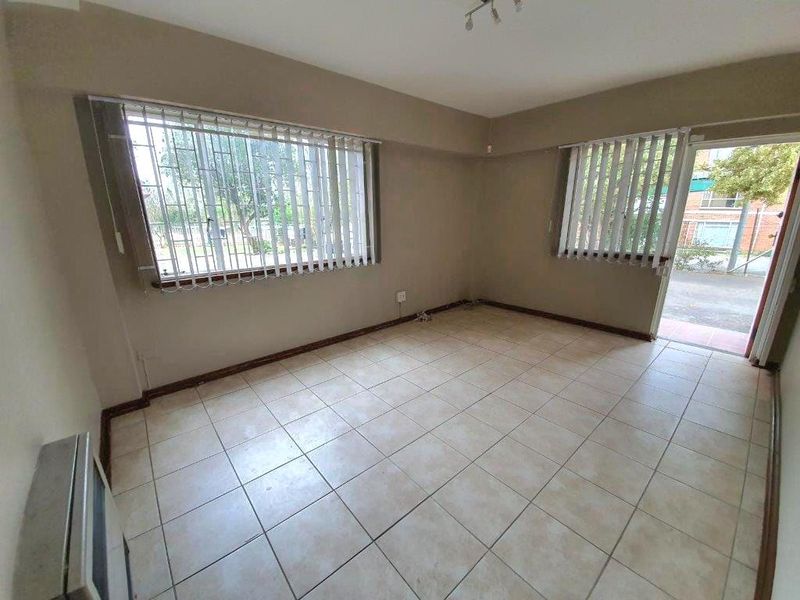 An empty living room featuring tiled flooring, security bars on windows, and a wall-mounted heater, offering a blank canvas for personalization.