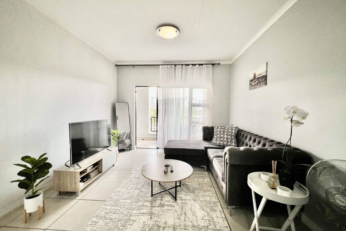 A bright living room featuring neutral tiled flooring and a sliding glass door providing access to an outdoor balcony area.