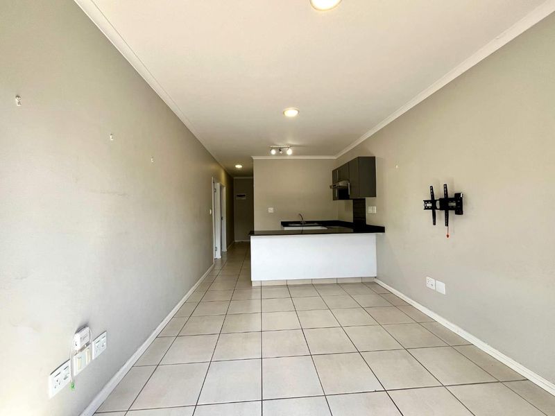 An open-plan living and kitchen area featuring tiled flooring, a compact kitchen island, and neutral wall finishes, presenting a blank canvas for potential residents.
